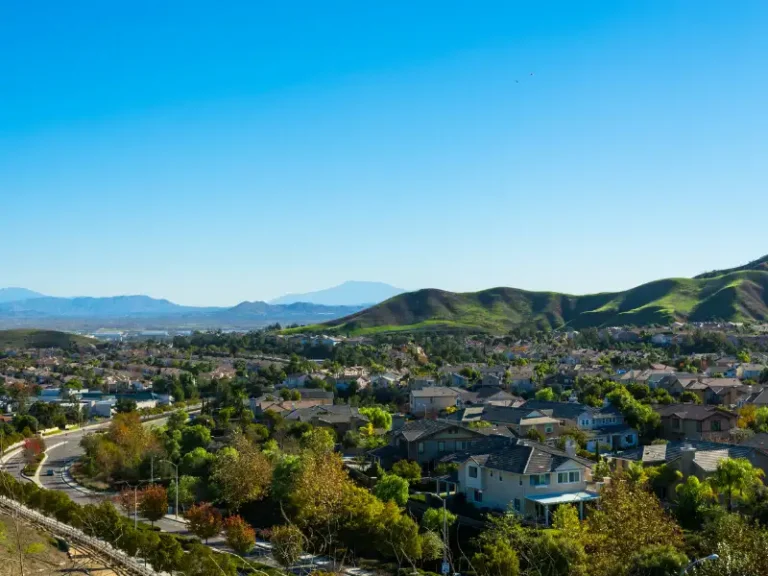 Suburban neighborhood with green hills under a clear blue sky.