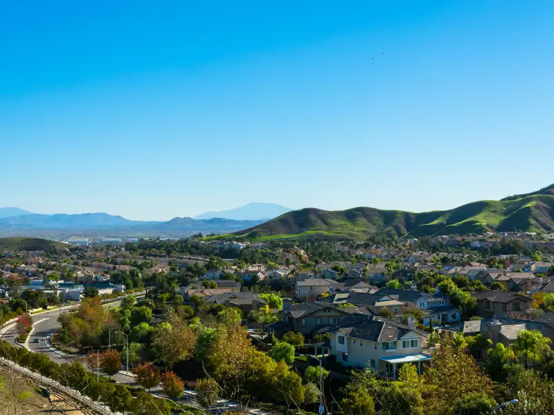 Suburban neighborhood with green hills under a clear blue sky.