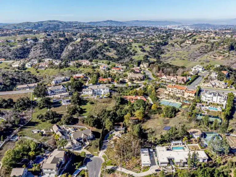 Aerial view of a suburban hillside neighborhood with houses and green hills.
