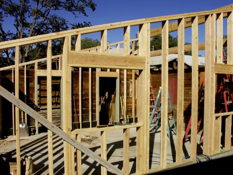 Wooden house framing under construction with ladders and tools.