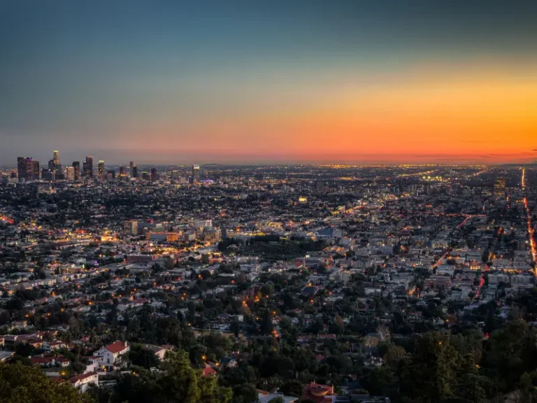 Sunset over a sprawling city skyline and glowing streets.