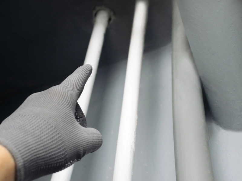 Gloved hand pointing at two white pipes in a gray utility space.