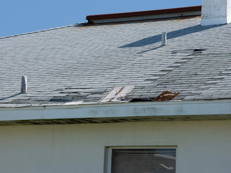 Damaged shingled roof with missing and torn sections.